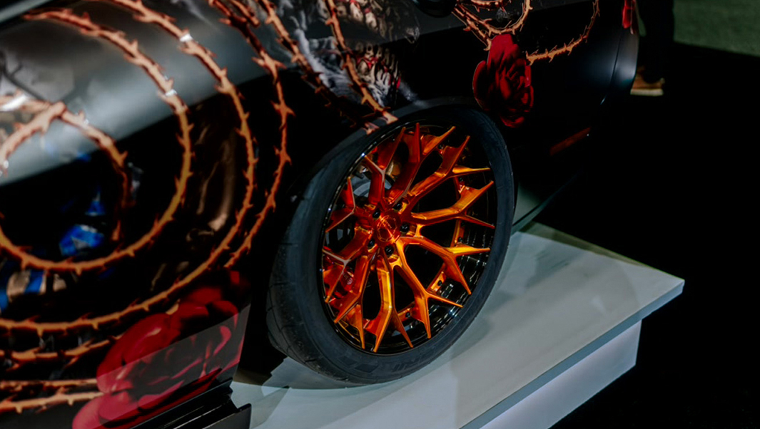 © Quelle: @orafolamericas Nahaufnahme einer extravaganten Car-Wrapping-Folie mit farblich passenden Felgen: Auf schwarzem Untergrund ranken sich feurig-glänzende rot-goldene Schlingen. | © Quelle: @orafolamericas